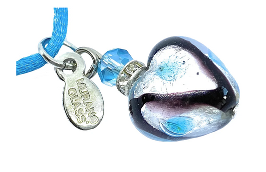 The Murano Passion Murano Glass Pendant, known as the Dainty 1.5cm Murano Heart Pendant, beautifully showcases a blue heart-shaped pendant adorned with enchanting swirls of blue, white, and dark hues. It is accompanied by a delicate bead and a metallic tag inscribed with "Murano Glass." This elegant piece of jewelry comes with a Certificate of Authenticity.