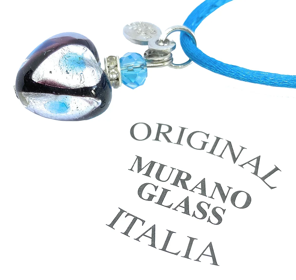 The Murano Passion Heart Pendant, a dainty 1.5cm piece crafted from exquisite Murano glass, elegantly hangs from a blue cord adorned with a mesmerizing interplay of blue and silver patches. It is complemented by small matching beads and comes with a Certificate of Authenticity that bears the legend: "Original Murano Glass Italia.