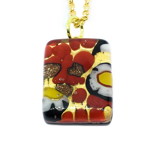 This stunning Murano Passion pendant, featuring a Millefiori Flower design on gold leaf, presents an elegant 2cm x 1.5cm glass piece adorned with abstract red, gold, black, and white patterns. The pendant glistens with shimmering elements and circular accents and is beautifully suspended from a gold-colored chain.