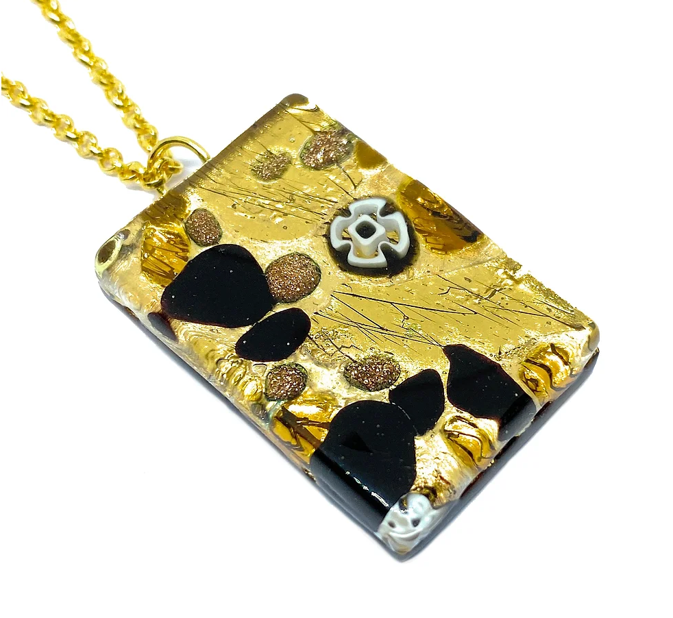 A rectangular Murano Glass Pendant, featuring a textured surface embellished with black and brown stones and adorned with a white floral design, elegantly hangs from a gold chain. This exquisite piece from the Murano Passion collection radiates elegance and comes with a Certificate of Authenticity.