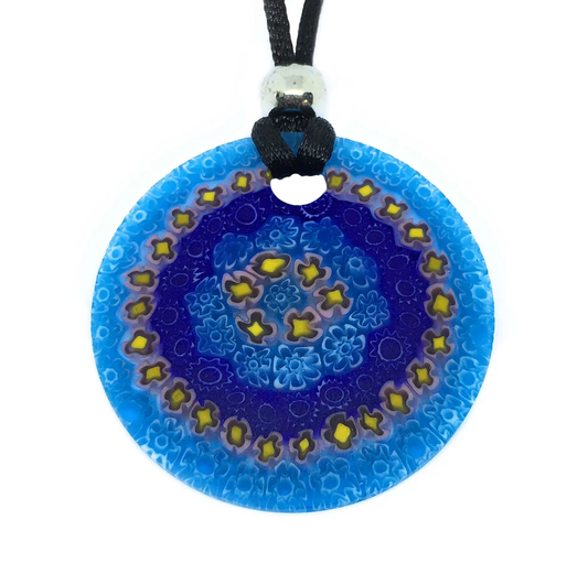 The Murano Passion Murano Glass Pendant, crafted with Millefiori Flowers and a 4cm diameter, features an intricate floral design in yellow and light blue on its round, blue surface. It hangs elegantly from a black cord accentuated by a silver bead near the top, reflecting the exquisite artistry of Venetian heritage with its symmetrical patterns and varying shades of blue.