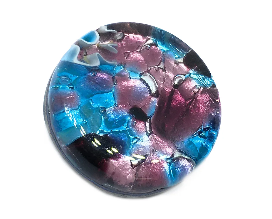 The Murano Passion brooch features a handmade, round design crafted from Murano glass, showcasing a marbled pattern in swirling shades of purple, blue, and hints of black. With its shiny surface on a silver leaf base measuring 2.4cm, it reflects intricate abstract designs reminiscent of millefiori pieces.