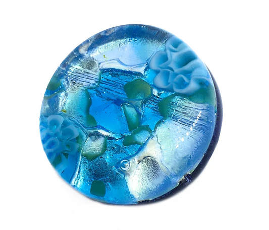 This exquisite Murano Passion brooch, evocative of Murano Glass craftsmanship, features a round blue form with a marbled texture adorned by abstract floral patterns in lighter blue and hints of green, all set on a 2.4cm silver leaf base.