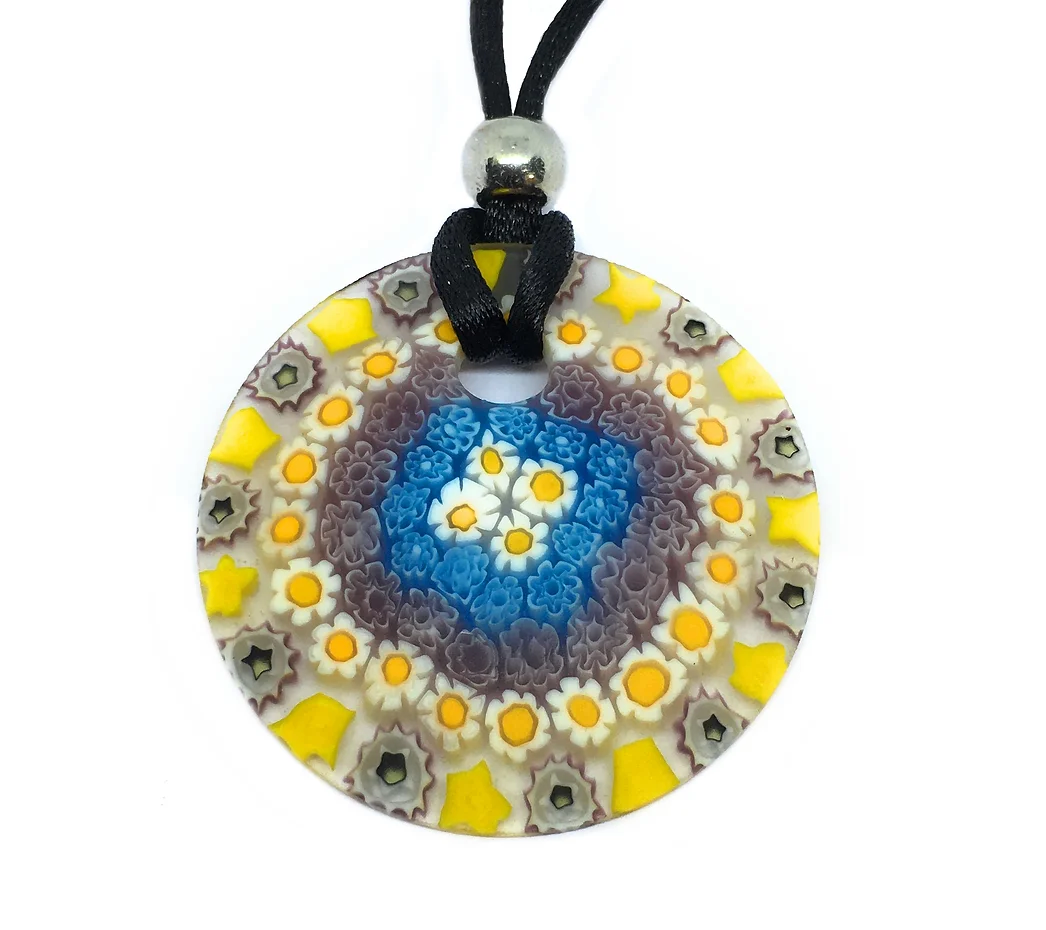 The Murano Passion pendant showcases intricate millefiori floral designs in blue, yellow, and brown. This piece of Venetian artistic heritage hangs on a black cord embellished with a silver bead and measures 4cm in diameter.