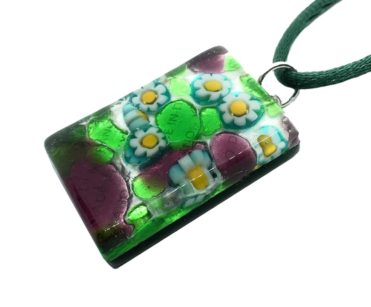 Introducing the Murano Passion Murano Glass Pendant, Millefiori Pendant on Silver Leaf, a 3cm x 2cm rectangular masterpiece featuring a green cord. This exquisite piece showcases intricate floral designs and geometric patterns in vibrant colors like green, purple, white, and yellow. Each expertly crafted piece of handmade jewelry is accompanied by a Certificate of Authenticity.