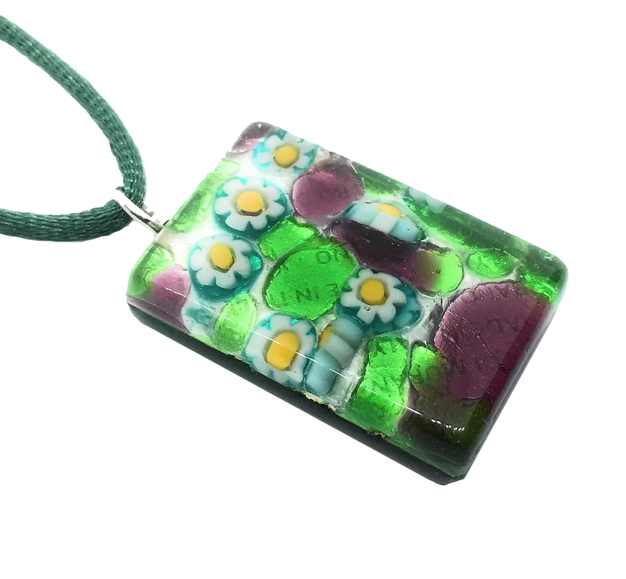 Introducing the Murano Glass Pendant by Murano Passion: a 3cm x 2cm Millefiori pendant on silver leaf, featuring a vibrant floral design. This handmade jewelry piece showcases blue and white flowers with yellow centers beautifully accented by green and purple hues. Each pendant comes with a Certificate of Authenticity.