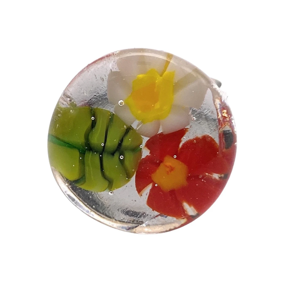 Presenting the elegant "Flower Ring" by Calon Glass, a handmade glass piece featuring a delicate white flower with a yellow center, a vivid red flower, and a charming striped green element, all beautifully encased in clear glass.