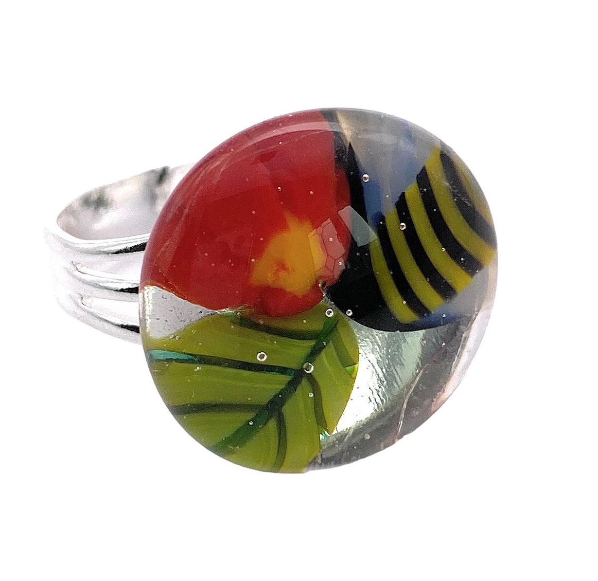 The handmade glass "Flower Ring" by Calon Glass (CGR3) features a vibrant Millefiori flower design, nestled within a shiny silver band. This colorful ring showcases a round, smooth surface with a striking red section and yellow center, complemented by a blue and yellow striped segment and a green leaf-like pattern.