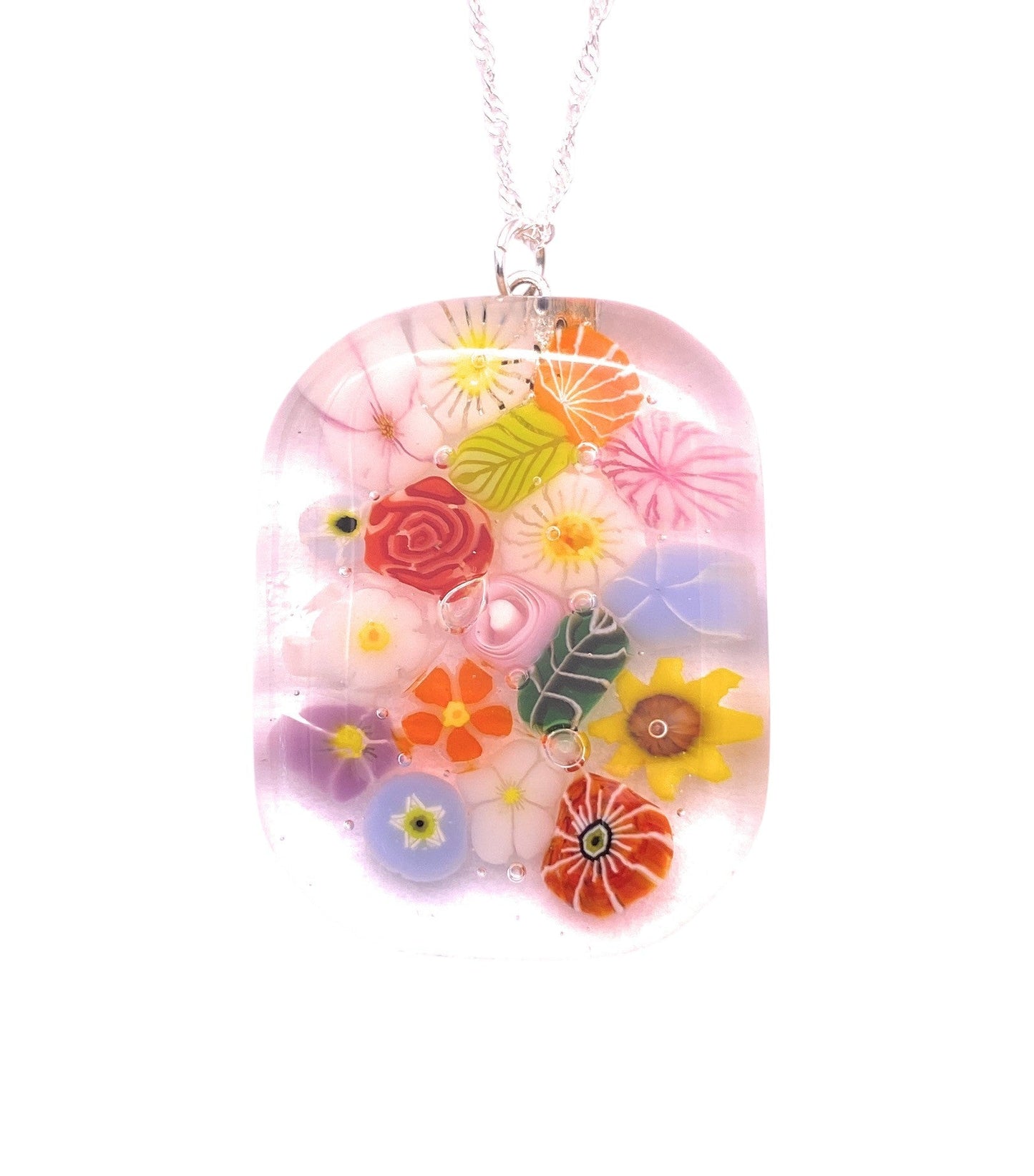 The Calon Glass Handmade Glass Pendant (CGP40) features a chunky 4cm x 3cm clear rounded rectangle with colorful Millefiori-inspired pink, yellow, red, and blue floral designs, encased in glass and hanging from a silver chain.