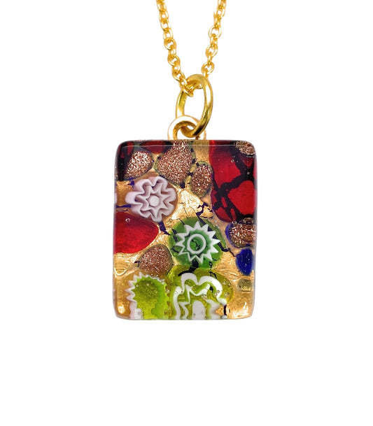 This Millefiori Flower Pendant by Murano Passion is a rectangular gem on a gold chain, showcasing an intricate mosaic design. With abstract patterns in red, green, white, and gold accents, it exudes a lively artistic flair. Each pendant measures a dainty 2cm x 1.5cm and comes with a Certificate of Authenticity to ensure its uniqueness.