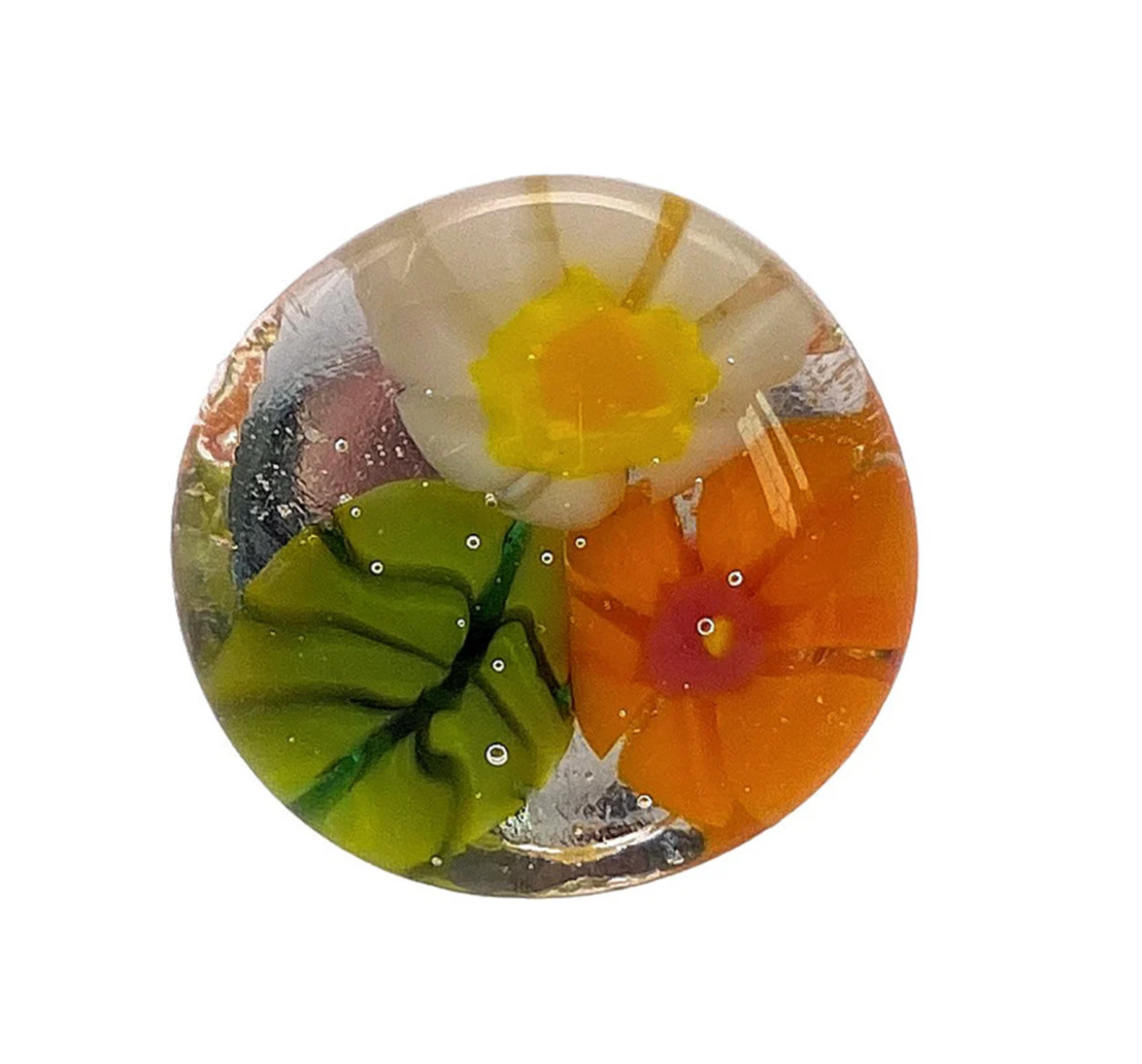 The Flower Ring by Calon Glass (CGR5) showcases a delicate millefiori-inspired design, featuring intricate arrangements of white and yellow flowers, an orange flower, and green leaves—all encased in clear handmade glass with charming small bubbles throughout.