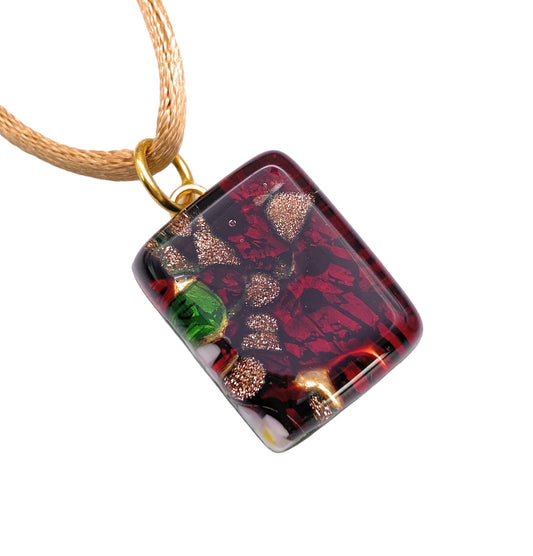 The Murano Passion Murano Glass Pendant, Red on Gold Leaf (MGPP14), features a dainty rectangular design decorated with a vibrant mosaic of red, gold, and green. Hanging gracefully from a light brown cord with a gold-colored loop, this elegant 2cm x 1.5cm piece comes with a Certificate of Authenticity to guarantee its genuine craftsmanship.